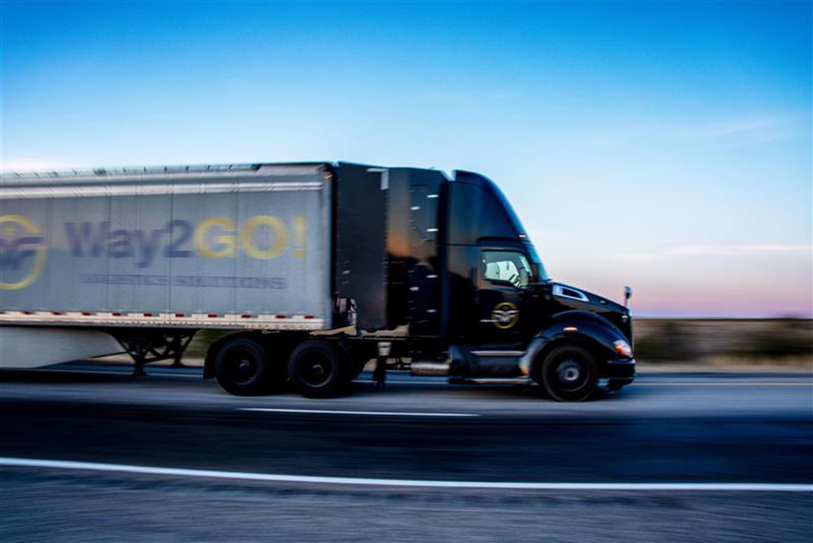 Black Way2GO! semi truck in motion at dusk showing speed and urgency